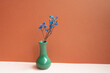 © Sanga - Green vase of blue dry flower on pink table. red background