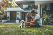 © BetterPhoto - A father and daughter playing with their small white dog on a well-manicured lawn in front of a modern house.