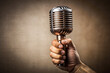 © Adisorn - Close-up of a solitary hand grasping a retro black wireless microphone with a sleek chrome grill and textured grip against a plain neutral background.