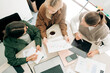 © Ilona - Top view of three business partners women working on a project while sitting at an office desk.