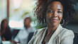 © Alina Tymofieieva - Portrait of a happy dark-skinned African American woman sitting at a desk in a work office. Young curly woman in business clothes indoors. Work concept. Lifestyle.