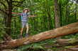 © Sergey Novikov - Teenager scout carefully balances on fallen log in a lush forest