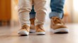 © Pinklife - A close-up shot of a toddler learning to walk with support from an adult, emphasizing the child's small feet and the adult's guidance on a hardwood floor.