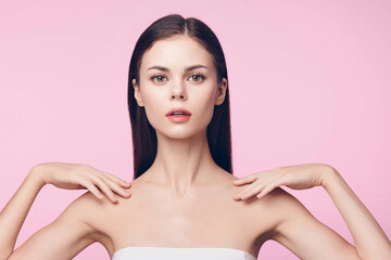 Poster - Beautiful young woman with hands on shoulders posing on pink background, showcasing flawless skin and beauty