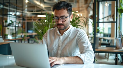 Poster - A man wearing glasses is sitting at a desk with a laptop open in front of him