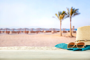 Sticker - Straw summer hat and sunglasses on a table with tropical summer holidays beach background. Copy space for products and objects and summer stuff.