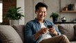 © Abi - A happy handsome Asian man checking social media on his smart phone while sitting on the sofa at home. The man smiled and seemed happy with his cell phone