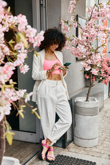 A woman in stylish attire explores the streets of Europe, enjoying the vibrant springtime beauty of cherry blossoms in full bloom.