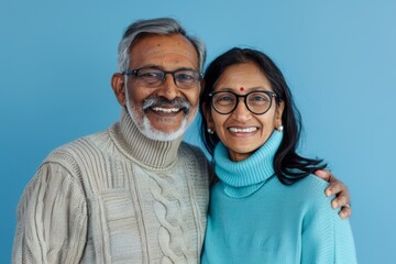 Wall Mural - Portrait of a glad indian couple in their 60s wearing a classic turtleneck sweater in front of pastel blue background