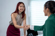 © Wasana - A woman shakes hands with another woman in a green jacket