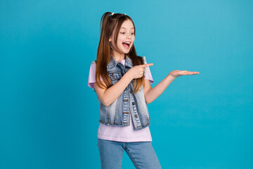 Wall Mural - Photo portrait of cute little girl headphones look hold point empty space dressed stylish denim clothes isolated on blue color background