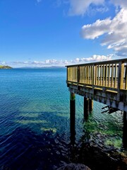 Wall Mural - Wooden pier extending over clear blue water under a blue sky. New Zealand, Whangarei Heads