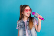© deagreez - Photo portrait of charming little girl sing karaoke sunglass wear trendy jeans outfit isolated on blue color background