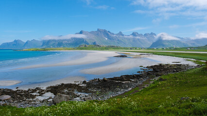 Wall Mural - a vast, sandy beach stretches out under a blue sky, bordered by green meadows and a range of mountai