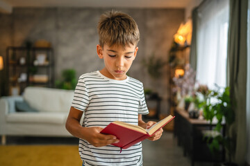 Portrait of young boy stand and hold, read book in the living room