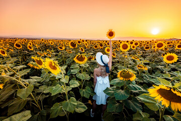 Woman in White Dress Holds Sunflower in Field at Sunset