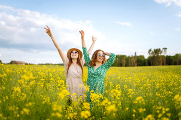 Wall Mural - Attractive two woman in the blooming field. Nature, vacation, relax and lifestyle. Summer landscape.