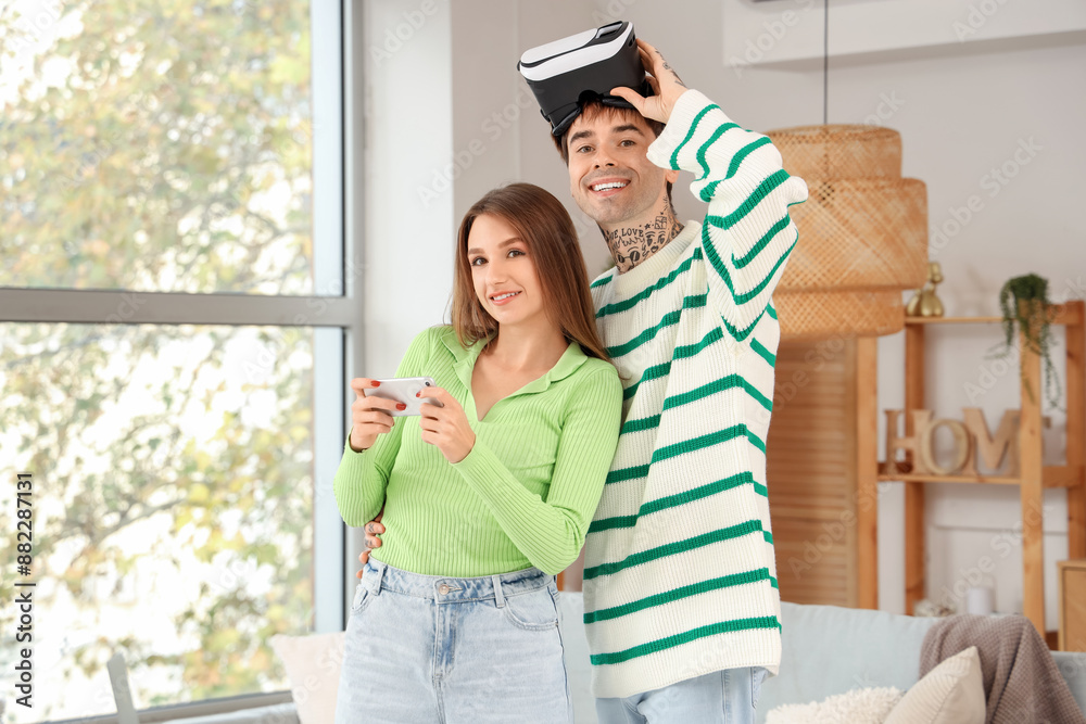 Young couple with mobile phone and VR glasses at home