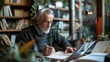 © Onzdemia - A senior man in glasses sits at a table in a coffee shop, focused on writing in a notebook. He is surrounded by books and greenery.