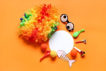 Wall Mural - Blank card with paper fish, clown wig and party decor on orange background. April Fools Day celebration