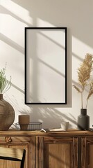 Sticker - An empty frame with a black border stands on a wooden cabinet, surrounded by pottery and a cup, bathed in sunlight and shadows, creating a calm, rustic ambiance.