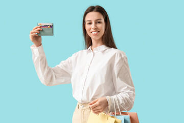 Sticker - Beautiful young woman with shopping bags and credit card holder on blue background