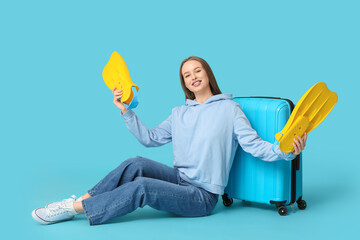 Sticker - Smiling young woman with suitcase and flippers on blue background. Travel concept