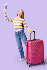 Sticker - Smiling young woman with suitcase, passport and ticket on lilac background. Travel concept