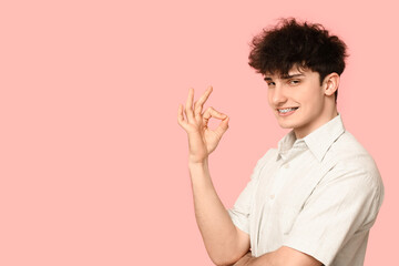 Poster - Smiling young man with dental braces showing OK on pink background