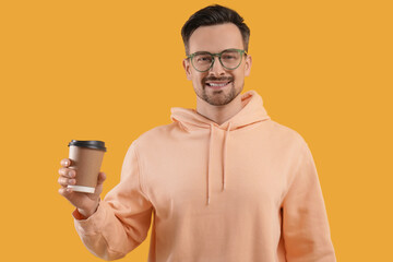 Wall Mural - Young man in eyeglasses with coffee to-go on yellow background