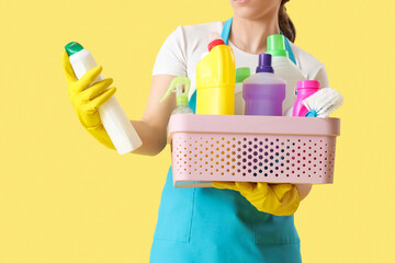 Poster - Female janitor with basket of cleaning supplies on yellow background, closeup