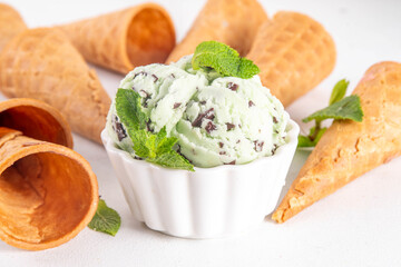 Wall Mural - Mint chocolate chip ice cream. Small portioned bowl with traditional mint and chocolate chips frozen gelato, with waffle cones on white table