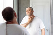 © Home-stock - Ingrown hair problem. Unshaved middle-aged man touching neck, looking at mirror in bathroom, making morning beauty routine