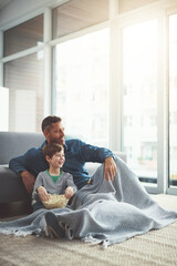 Poster - Popcorn, laugh and father watching tv with child on floor in living room at family home. Blanket, relax and dad with boy kid for streaming movie, film or show with snack in lounge at house in Canada.