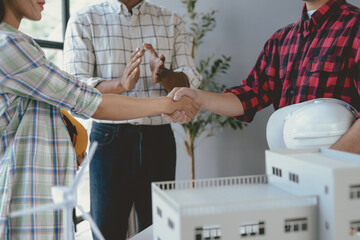 Wall Mural - Two architects shake hands joyfully in a busy office, with a colleague clapping in the background. Happy teamwork as they plan their next project