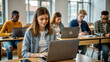 © NewFresh  - Young female student using laptop in classroom with group of students in background