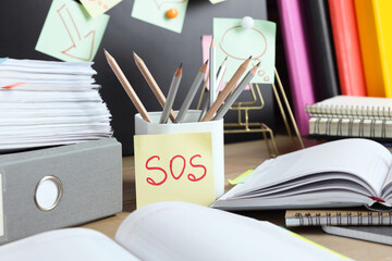 Sticky note with word SOS and stationery on table at workplace