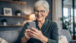 © NewFresh  - happy senior woman in eyeglasses using smartphone while sitting on sofa at home