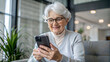 © NewFresh  - Smiling senior woman using mobile phone at home in the living room