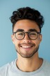 © Enigma - Young man with curly hair and glasses smiles happily on a blue background, radiating positivity and joy