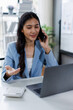 © David - Happy asian business woman working on laptop, using mobile phone at modern office, analyzing business document with financial graph, market report on digital tablet, business data analysis concept