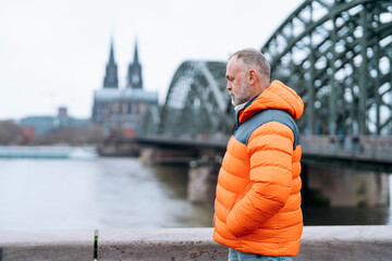 Sad Man in Orange Puffer Jacket Stands by River in Hamburg