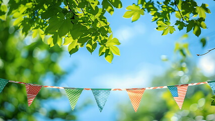 Fototapete - A string of colorful triangle flags hangs from a tree with green leaves.