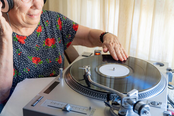 Canvas Print - Older woman listening music with vinyl records on a turntable.