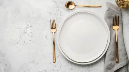 A simple table setting featuring two gold forks, a knife, and a spoon on a white napkin, with two white plates on a grey surface