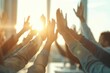 © justjupiter - Group of people raising hands in a bright meeting room, sunlit atmosphere symbolizing teamwork and collaboration during a workshop session.