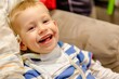 © Svyatoslav Lypynskyy - A young boy with a tracheostomy tube smiles brightly while sitting on a couch, radiating pure joy and infectious happiness.