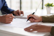 © STBSTD - Close-up of two individuals discussing and pointing at a document on a desk. The hands are holding pens, indicating a review or collaboration on the content of the document