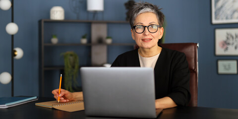 Sticker - A woman is sitting at a desk with a laptop and a pencil. She is wearing glasses and a black jacket