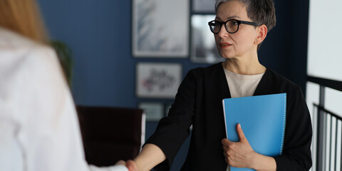 Sticker - A woman shakes hands with another woman in a business setting. The woman on the left is wearing a white shirt